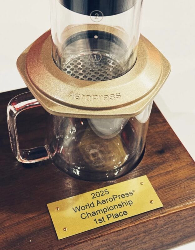 2025 World AeroPress Championship first-place trophy: a gold AeroPress brewer mounted on a walnut base with an engraved plaque