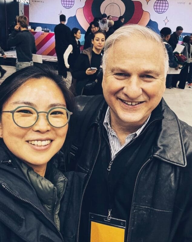 Monica Lim posing for a selfie with a man at the World AeroPress Championship venue, colorful event branding behind them