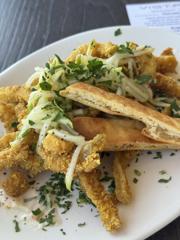 Plate of crispy fried calamari strips topped with shaved fennel, herbs, and flatbread on a restaurant table