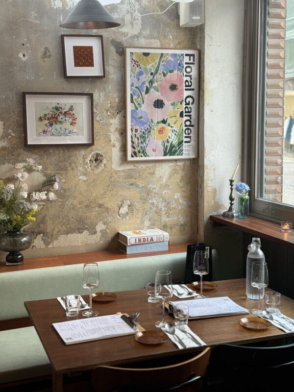 Restaurant dining room with distressed plaster walls, framed art, a Floral Garden poster, and set tables beside a window