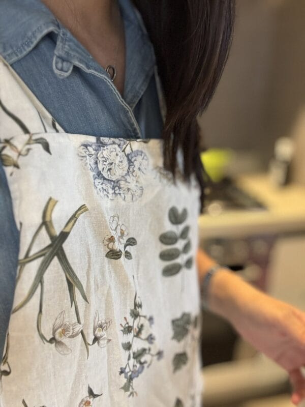 Close-up of a floral linen apron worn over a denim shirt, kitchen counter blurred in the background